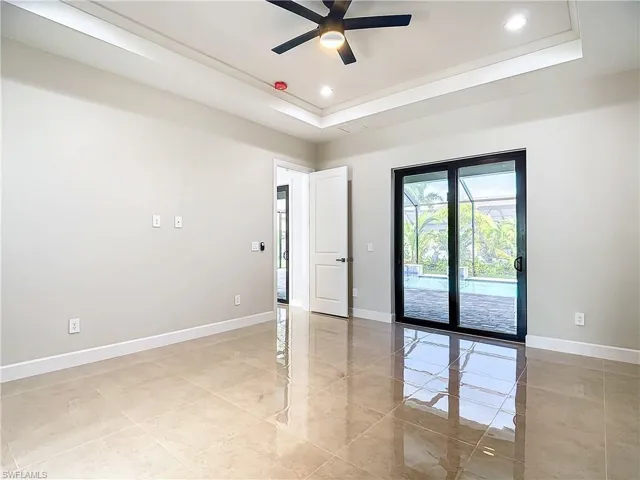 Empty room featuring a tray ceiling, ceiling fan, and light tile floors