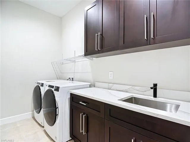 Washroom with cabinets, washing machine and clothes dryer, hookup for a washing machine, sink, and light tile flooring
