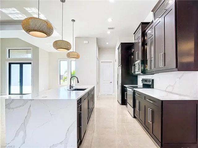 Kitchen with hanging light fixtures, appliances with stainless steel finishes, sink, tasteful backsplash, and light tile floors