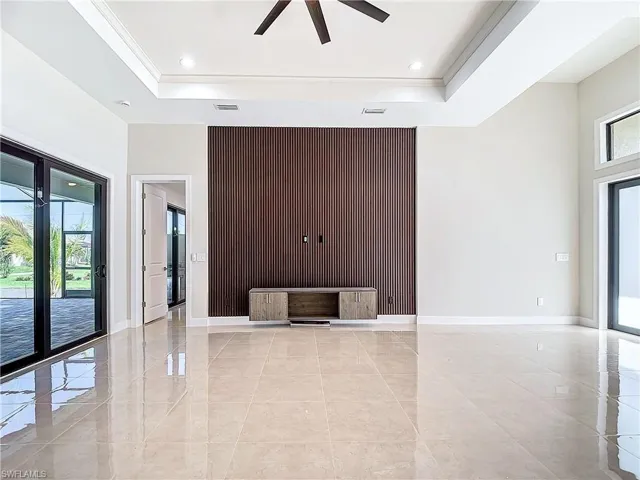Unfurnished living room featuring ceiling fan, a tray ceiling, light tile flooring, and a wealth of natural light