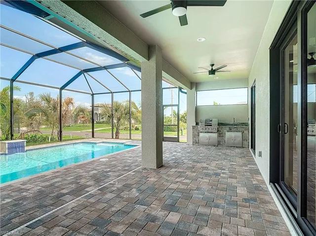 View of swimming pool with ceiling fan, area for grilling, an outdoor kitchen, a patio area, and glass enclosure