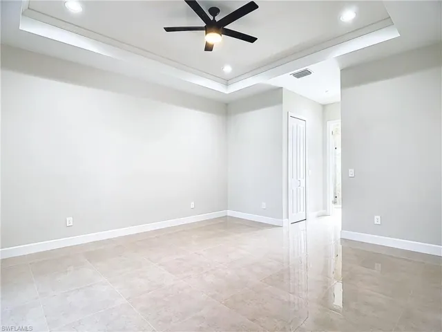 Empty room featuring ceiling fan, a tray ceiling, and light tile floors