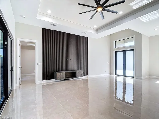 Unfurnished living room with a tray ceiling, ceiling fan, french doors, and light tile floors