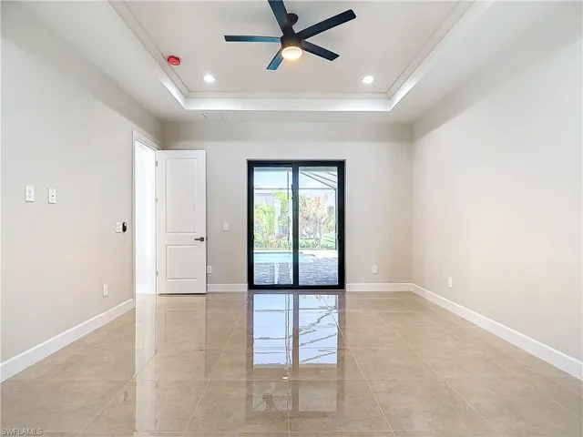 Empty room with a tray ceiling, ceiling fan, and light tile floors