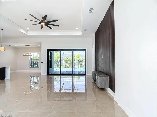 Unfurnished living room with a raised ceiling, ceiling fan, and light tile floors