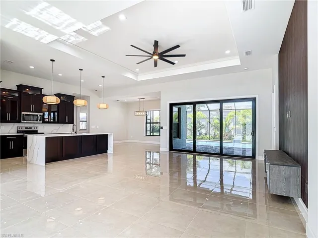 Kitchen featuring hanging light fixtures, stainless steel appliances, a raised ceiling, and a center island with sink