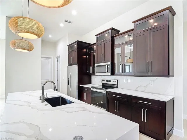 Kitchen featuring light stone countertops, tasteful backsplash, stainless steel appliances, decorative light fixtures, and sink