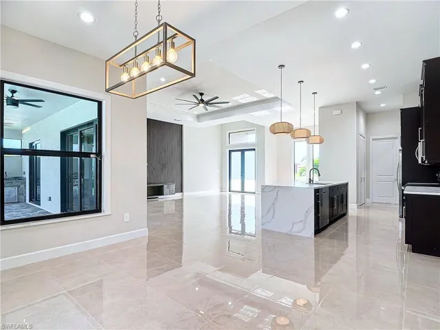 Kitchen featuring ceiling fan with notable chandelier, hanging light fixtures, a kitchen island with sink, sink, and light tile floors