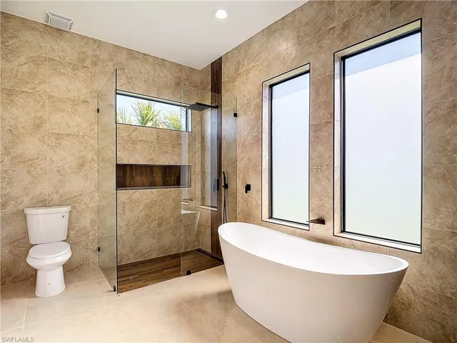 Bathroom with tile floors, independent shower and bath, toilet, and tile walls