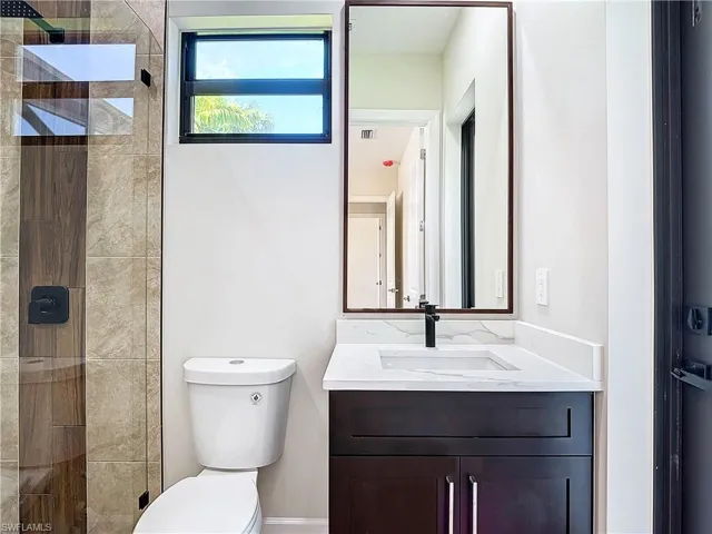 Bathroom with tiled shower, vanity with extensive cabinet space, and toilet