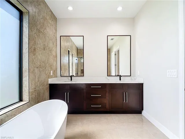 Bathroom featuring tile walls, oversized vanity, dual sinks, tile flooring, and a bath