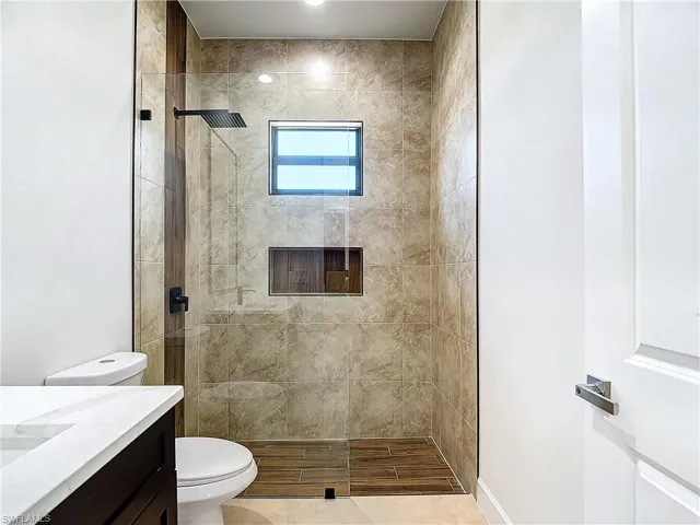 Bathroom with tiled shower, tile floors, vanity, and toilet