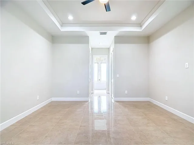 Tiled empty room featuring ceiling fan and a tray ceiling
