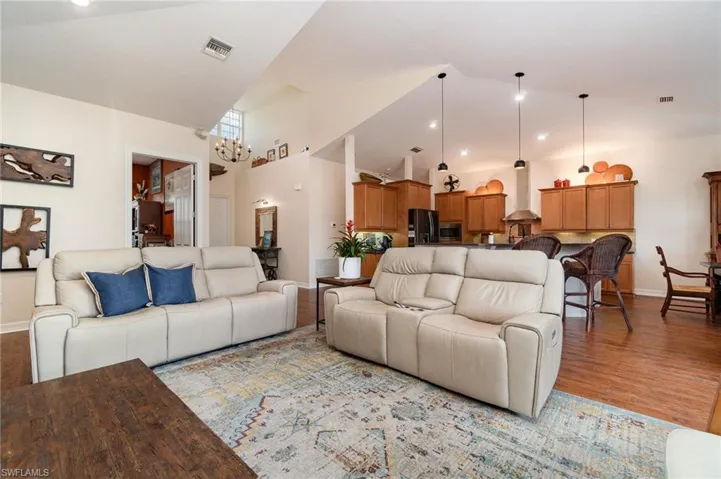 Living area with high vaulted ceiling, baseboards, a chandelier, light wood finished floors, and visible vents