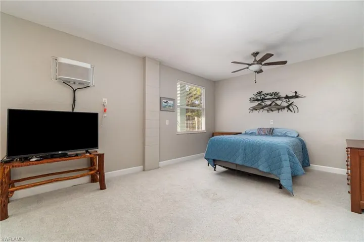 Carpeted bedroom featuring baseboards, an AC wall unit, and a ceiling fan