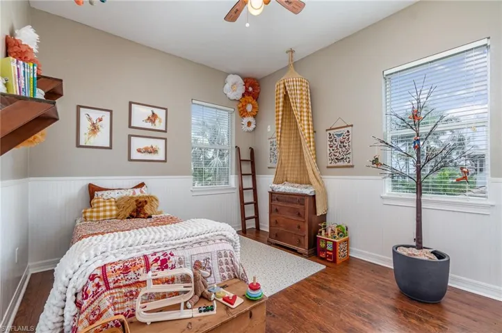 Bedroom featuring ceiling fan, wood finished floors, and wainscoting