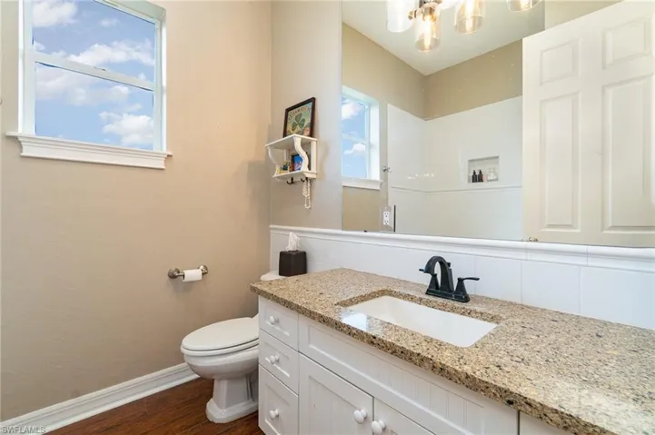 Full bathroom with toilet, vanity, wood finished floors, baseboards, and an inviting chandelier