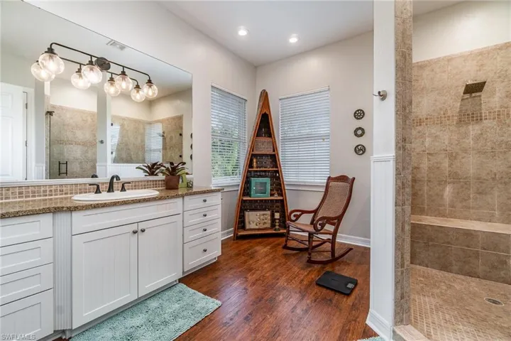 Bathroom featuring a tile shower, vanity, wood finished floors, baseboards, and recessed lighting
