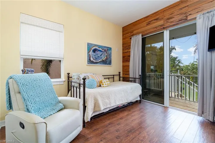 Bedroom with multiple windows, access to outside, wooden walls, and wood-type flooring
