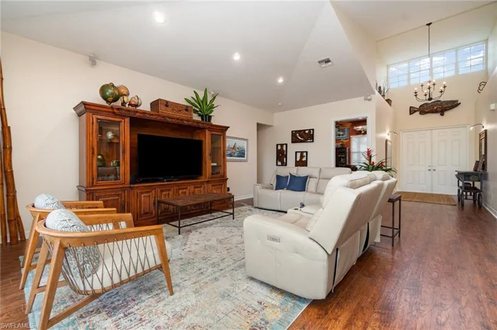 Living area with visible vents, a notable chandelier, high vaulted ceiling, and wood finished floors
