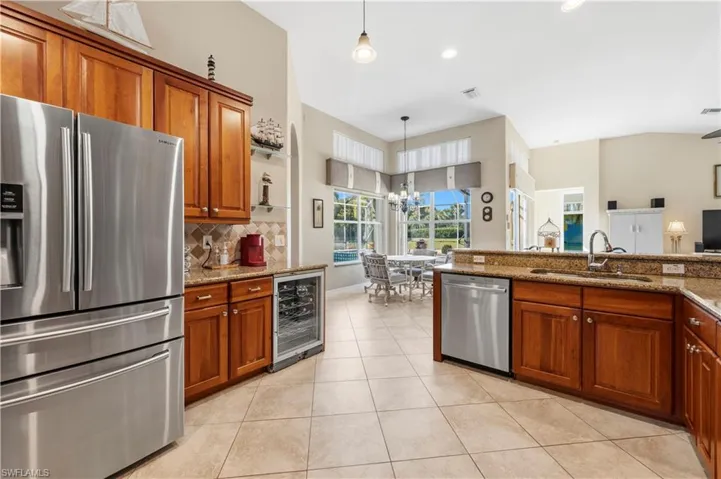 Kitchen featuring stainless steel appliances, wood finish cabinets, beverage cooler, light tile patterned floors, and light stone countertops