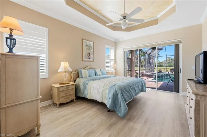 Bedroom featuring ornamental molding, light wood-style floors, access to outside, a tray ceiling, and a ceiling fan