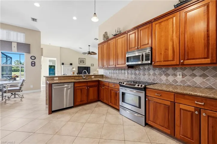 Kitchen featuring wood finish cabinets, stainless steel appliances, dark stone counters, light tile patterned floors, and vaulted ceiling