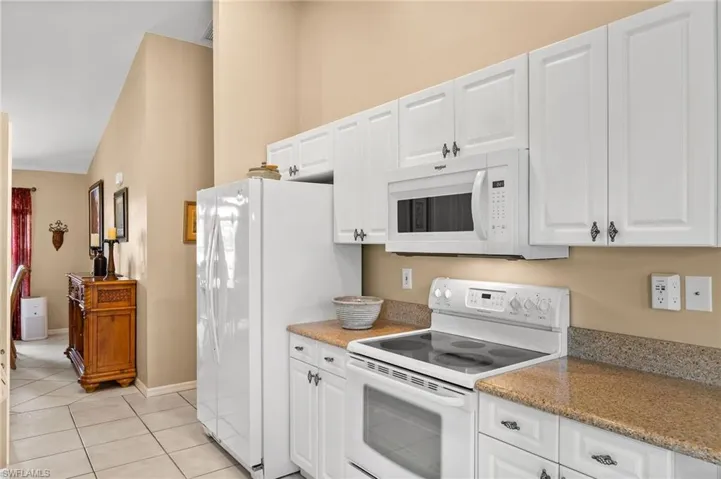 Kitchen featuring white appliances, vaulted ceiling, white cabinetry, and light tile patterned floors
