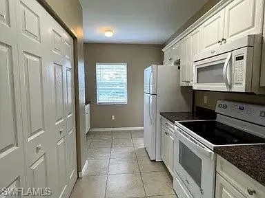 Kitchen with baseboards, white appliances, and white cabinets