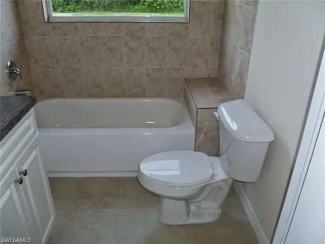 Bathroom featuring tile patterned flooring, a healthy amount of sunlight, toilet, and a tub to relax in