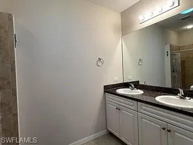 Full bath featuring a sink, baseboards, double vanity, and a tile shower