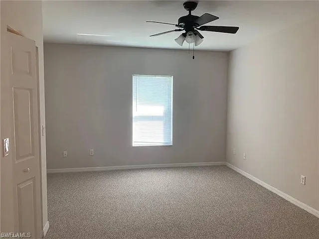 Carpeted empty room featuring a ceiling fan and baseboards