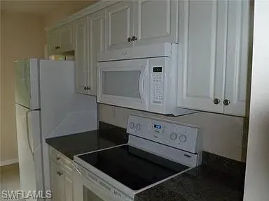 Kitchen featuring white appliances, white cabinets, and dark countertops