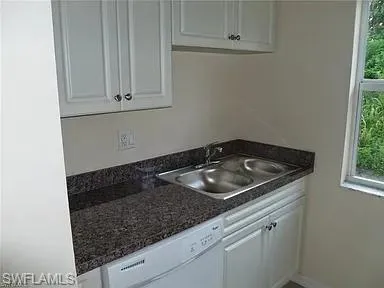 Kitchen featuring a sink, baseboards, white dishwasher, and white cabinetry