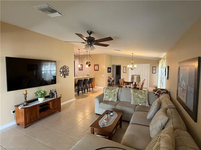 Living area featuring ceiling fan, light tile patterned flooring, lofted ceiling, and a chandelier