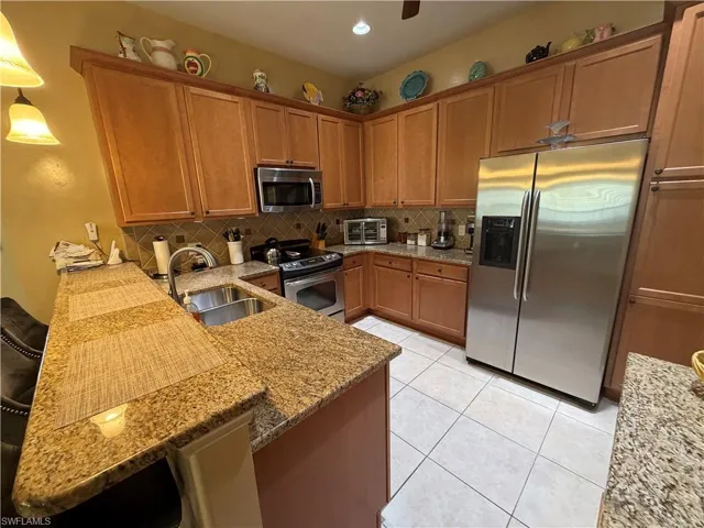 Kitchen with brown cabinetry, stainless steel appliances, light stone counters, tasteful backsplash, and pendant lighting