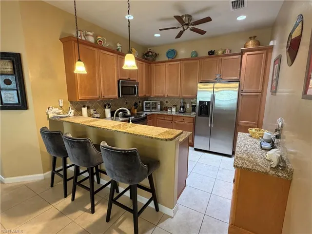 Kitchen with a peninsula, stainless steel appliances, a breakfast bar, decorative light fixtures, and brown cabinetry