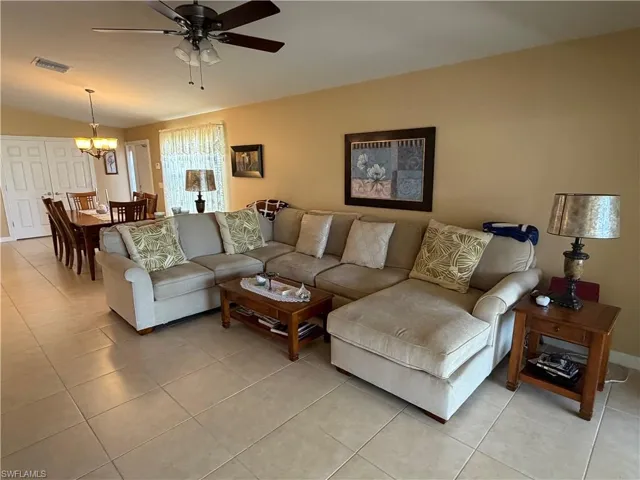 Living area featuring light tile patterned flooring, ceiling fan, lofted ceiling, and a chandelier