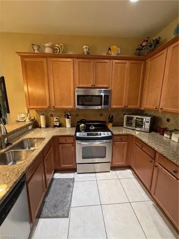 Kitchen featuring brown cabinets, stainless steel appliances, light stone counters, and light tile patterned floors