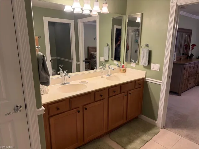 Ensuite bathroom with double vanity, light carpet, light tile patterned floors, and ornamental molding