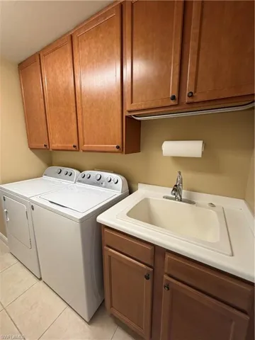 Laundry area featuring washing machine and dryer, cabinet space, and light tile patterned floors