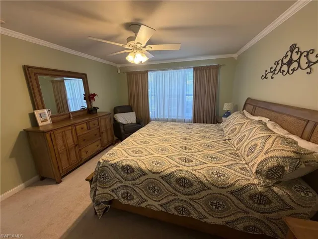 Bedroom with light colored carpet, crown molding, and ceiling fan