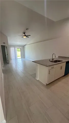 Kitchen featuring white cabinetry, lofted ceiling, light stone countertops, open floor plan, and a ceiling fan