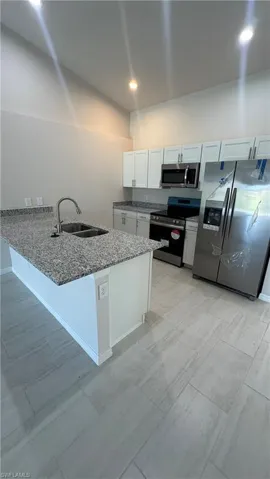 Kitchen featuring stainless steel appliances, light stone countertops, white cabinets, a peninsula, and recessed lighting