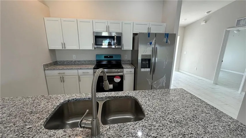 Kitchen with appliances with stainless steel finishes, light stone countertops, and white cabinets