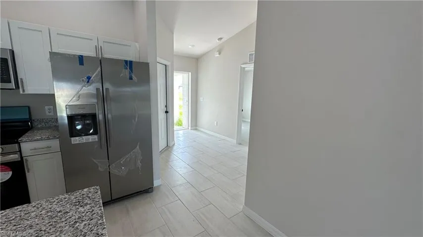 Kitchen with stainless steel appliances, light stone countertops, white cabinetry, and wood finish floors