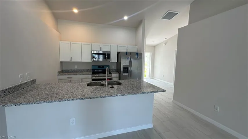 Kitchen featuring light stone countertops, stainless steel appliances, white cabinets, a peninsula, and wood tiled floors