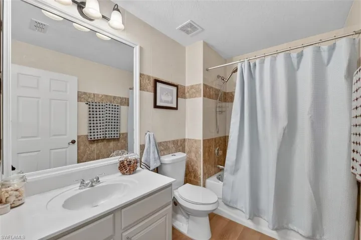 Full bathroom featuring vanity, shower / tub combo with curtain, a textured ceiling, tile walls, and light wood-style floors