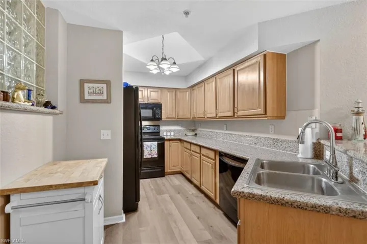 Kitchen featuring hanging lights, a textured wall, black appliances, light wood-style floors, and light stone countertops