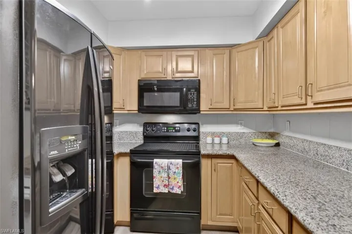 Kitchen with black appliances, light stone countertops, and light wood finish cabinetry